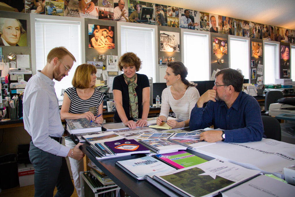 Eisterhold Associates team of five collaborating around a studio work table covered in exhibit design materials, Kansas City