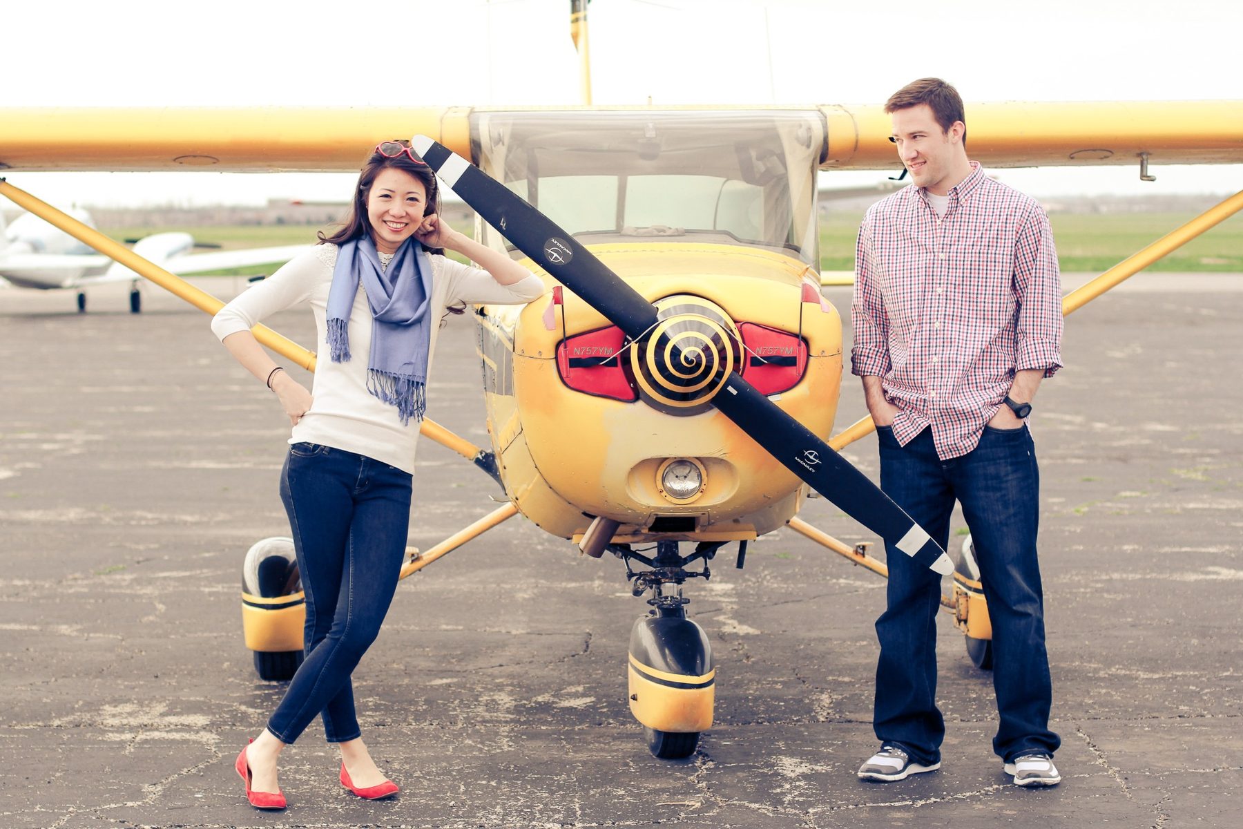 An engaged couple standing beside a yellow airplane on the airfield.