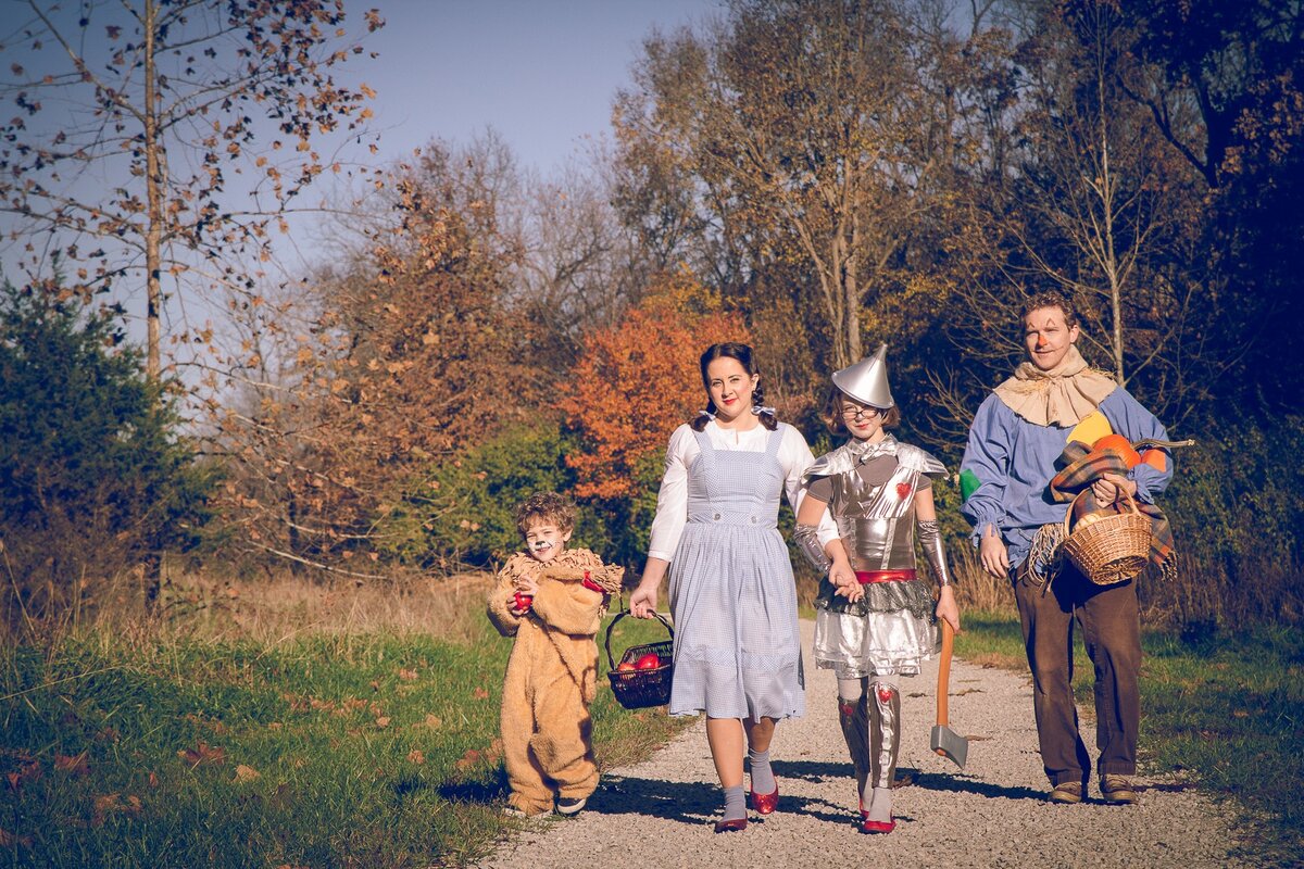 A family dressed as the Scarecrow, Tin Man, Dorothy, and Cowardly Lion beside a woodland path.
